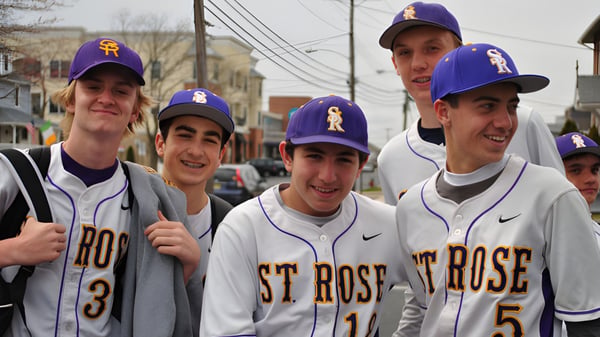 Eine Gruppe Schüler der St. Rose High School steht zusammen auf einem Gehweg und trägt lila Baseballcaps und Trikots.