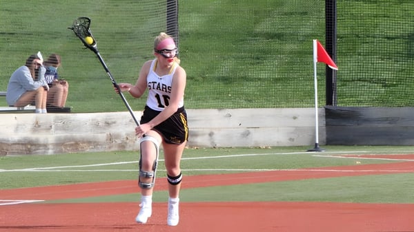 Eine Person in rosa Trikot steht auf dem Baseballfeld des St. Teresa’s College mit grünem Gras und rotem Lehmboden.
