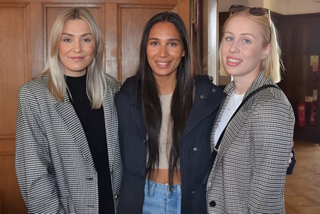 Drei Schülerinnen posieren vor einer Holzwand auf dem Campus von St. Teresa’s College.