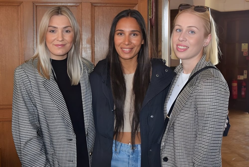Drei Schülerinnen posieren vor einer Holzwand auf dem Campus von St. Teresa’s College.
