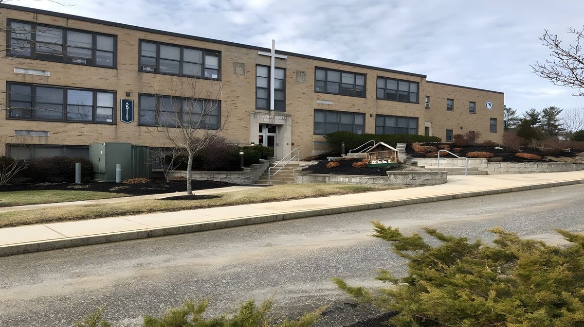 Das mehrstöckige Backsteingebäude der St. Thomas Aquinas High School mit großen Fenstern an einer baumgesäumten Straße.