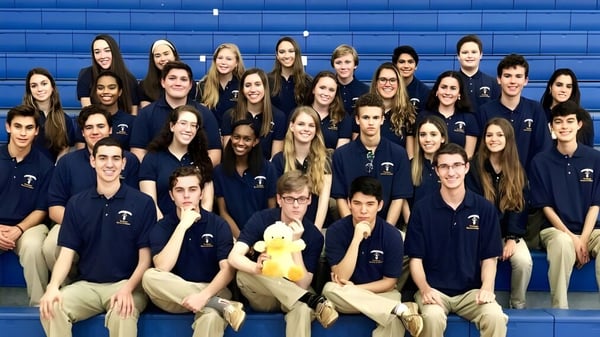 Eine Gruppe von Schülerinnen und Schülern der St. Thomas Aquinas High School posiert vor einer blauen Wand in einheitlichen dunkelblauen Shirts.