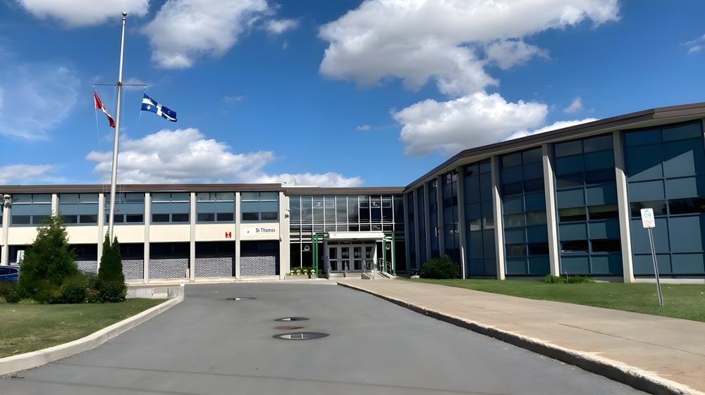 Das moderne mehrstöckige Gebäude der St. Thomas High School mit Glaswänden und gepflasterter Zufahrt bei blauem Himmel.