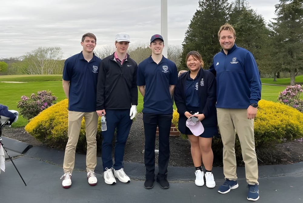 Eine Gruppe von Schülern der St. Thomas More School steht gemeinsam im Park mit Bäumen und Grünflächen im Hintergrund.