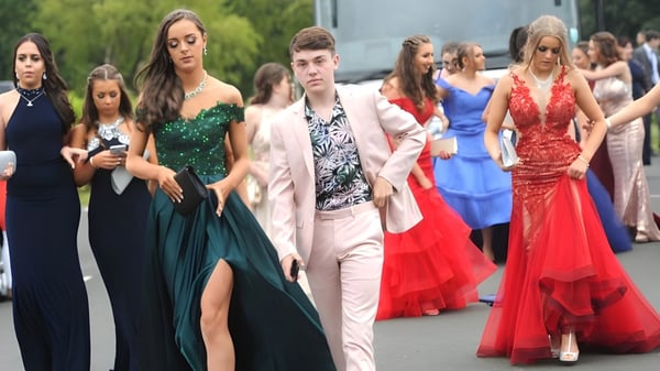 Eine Gruppe elegant gekleideter Schülerinnen und Schüler von St. Tiernan’s College versammelt sich im Freien vor Bäumen und Gebäuden.