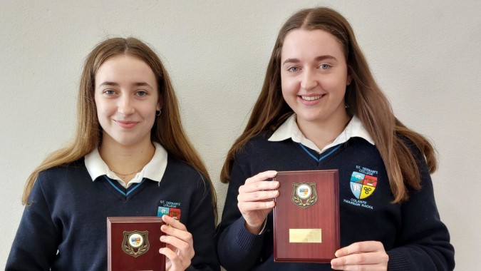 Zwei Schülerinnen des St. Tiernan’s College halten stolz Auszeichnungen in den Händen.