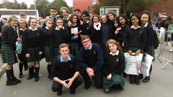 Eine große Gruppe von Schülerinnen und Schülern der St. Tiernan’s College steht gemeinsam vor einem Schulgebäude im Freien.