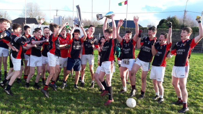 Schüler von St. Tiernan’s College feiern ihren Sieg auf dem Sportfeld mit Sportgeräten im Hintergrund.