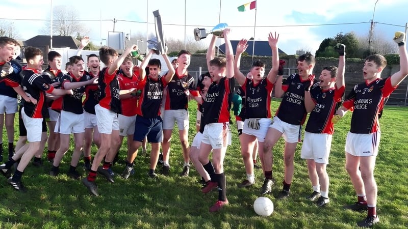 Schüler des St. Tiernan’s College feiern gemeinsam in ihren Sportuniformen auf einem Sportfeld mit Stadion im Hintergrund.