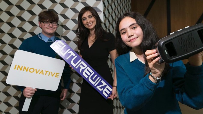 Drei Personen stehen vor einer gemusterten Wand und halten auf dem Campus der St. Tiernan’s Community School ein Schild mit der Aufschrift Innovative.