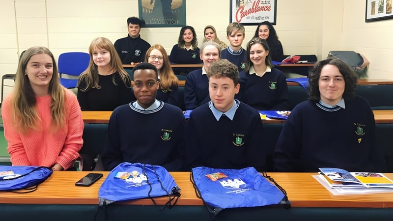 Schüler der St. Tiernan’s Community School sitzen in Schuluniformen an Tischen mit Schulmaterialien.