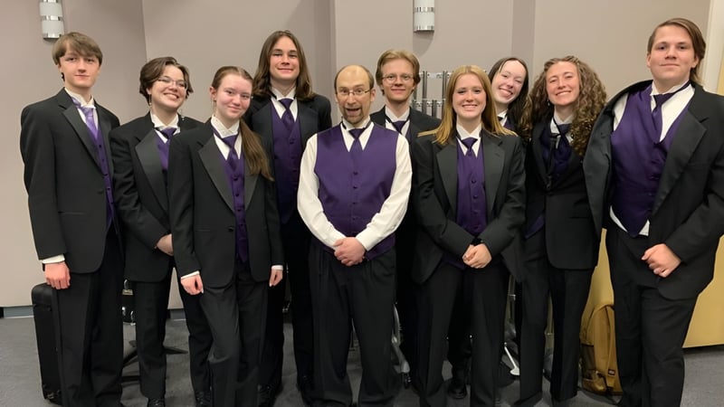 Eine Gruppe von Schülerinnen und Schülern der St. Timothy High School steht in formeller Kleidung als Chor in einem Raum mit weißen Wänden.