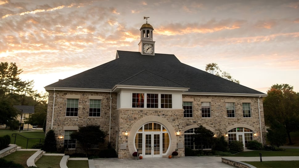 Das historische Gebäude mit Uhrturm auf dem Campus der St. Timothy's School vor einem Sonnenuntergangshimmel.