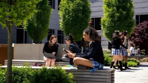 Eine Gruppe von Schülerinnen und Schülern sitzt auf Bänken im Außenbereich auf dem Gelände der St. Timothy's School.