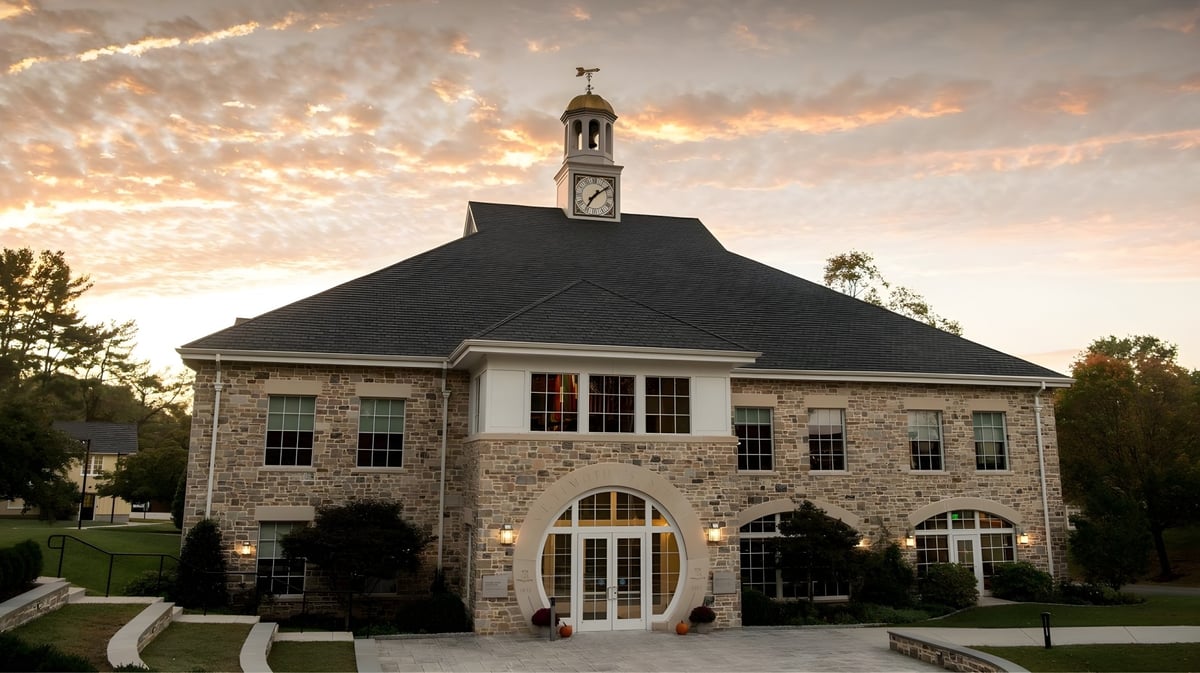 Das Gebäude mit Uhrturm von St. Timothy's School ist von einer gepflegten Anlage umgeben und wird von einem Sonnenuntergang beleuchtet.