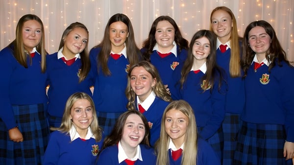 Eine Gruppe Schülerinnen in blauen Uniformen mit roten Akzenten posiert vor funkelndem Hintergrund auf dem Campus von St. Vincent's Secondary School.
