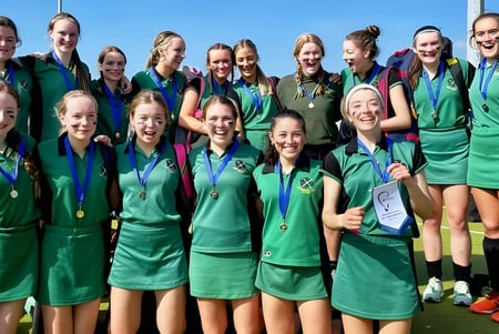 Eine Gruppe junger Athletinnen der St. Vincent's Secondary School feiert gemeinsam ihren Erfolg vor klarem blauem Himmel.