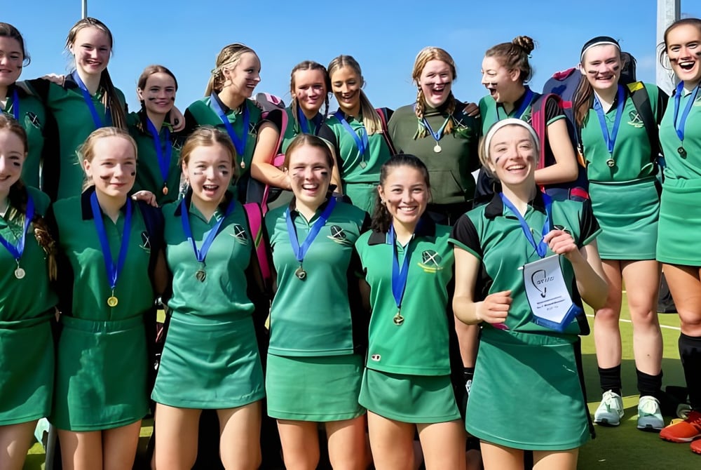 Eine Gruppe junger Athletinnen der St. Vincent's Secondary School feiert gemeinsam ihren Erfolg vor klarem blauem Himmel.