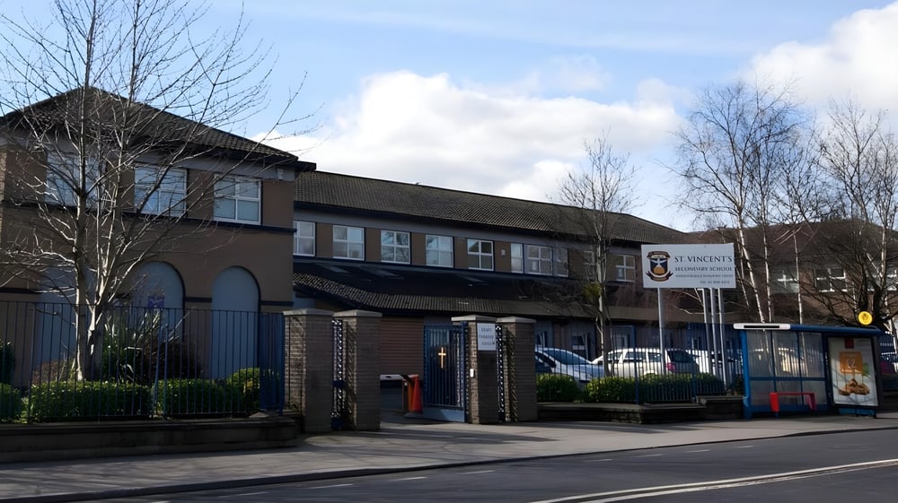 Das mehrstöckige Backsteingebäude der St. Vincent's Secondary School mit Fenstern und einem Schild steht an einer Straße, umgeben von Bäumen.