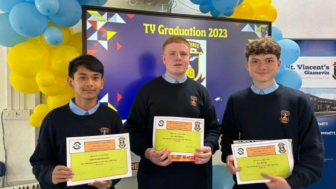 Drei Schülerinnen und Schüler der St. Vincent's Secondary School in Dublin halten Zertifikate vor einer Kulisse mit dem Schriftzug TV Graduation 2023.