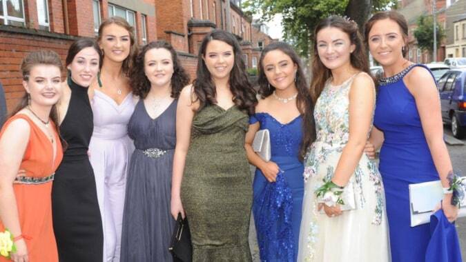 Eine Gruppe junger Frauen in formeller Kleidung posiert auf einer Stadtstraße vor Backsteingebäuden auf dem Campus der St. Vincent's Secondary School.