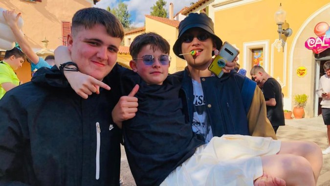 Drei Schüler der St. Vincent's Secondary School in Dublin stehen gemeinsam in einem farbenfrohen Außenbereich mit Gebäuden im Hintergrund.