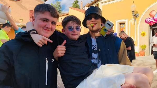 Drei Schüler stehen auf dem Außengelände der St. Vincent's Secondary School in Dublin vor farbenfrohen Gebäuden.