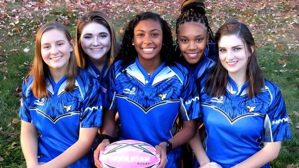 Eine Gruppe von fünf Schülerinnen der St. Vincent's Secondary School posiert im blauen Sportdress auf einem Feld mit buntem Herbstlaub.