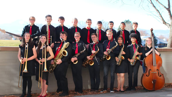Eine Gruppe von Musikern in formeller Kleidung posiert mit ihren Instrumenten vor einem Gebäude auf dem Campus der St. Vrain Valley Schools.