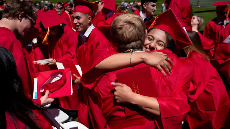 Eine Gruppe von Absolventen in roten Roben umarmt sich auf einer Wiese auf dem Campus der St. Vrain Valley Schools.