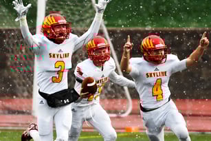 Drei Footballspieler in weißen Uniformen mit roten Helmen feiern auf dem nassen Spielfeld der St. Vrain Valley Schools.
