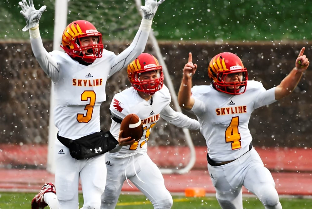 Drei Footballspieler in weißen Uniformen mit roten Helmen feiern auf dem nassen Spielfeld der St. Vrain Valley Schools.