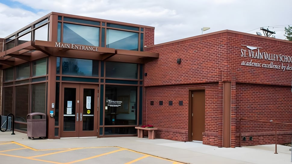 Das Backsteingebäude mit Haupteingang der St. Vrain Valley Schools steht vor bewölktem Himmel und ist von einem gepflasterten Bereich umgeben.