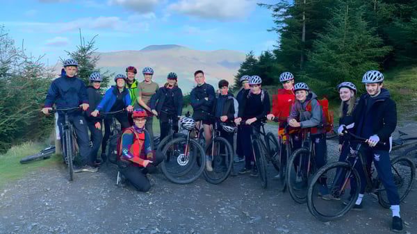 Eine Gruppe von Schülern der Stamford Endowed Schools steht in Radfahrerbekleidung auf einem Waldweg mit Kiefern und Bergen im Hintergrund.