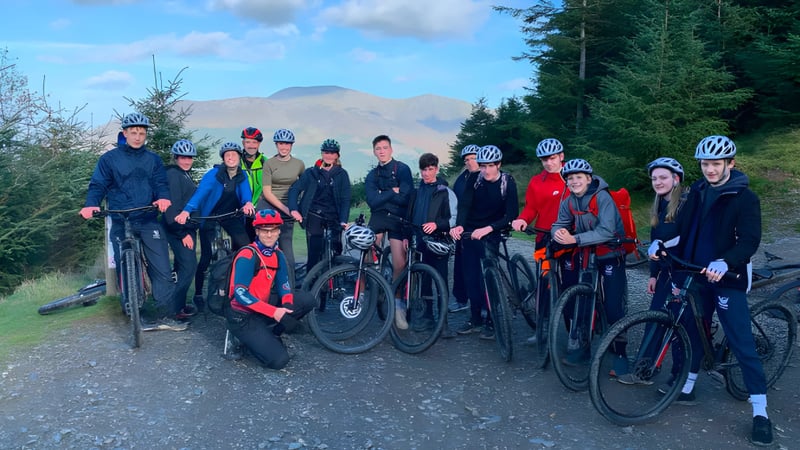 Eine Gruppe von Schülern der Stamford Endowed Schools steht in Radfahrerbekleidung auf einem Waldweg mit Kiefern und Bergen im Hintergrund.