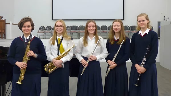 Fünf Schülerinnen in Schuluniformen der Stamford Endowed Schools stehen gemeinsam mit einer Flötenspielerin vor einem Projektionsschirm.