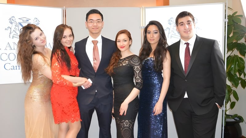 Sechs Personen posieren bei einer Veranstaltung auf dem Campus von St. Andrew’s College Cambridge vor einem AMCHAM-Hintergrund.