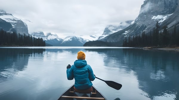 Eine Person in blauem Jacke und Hut paddelt ein Kanu auf einem spiegelglatten See mit verschneiten Bergen im Hintergrund auf dem Campus der Stanstead College.