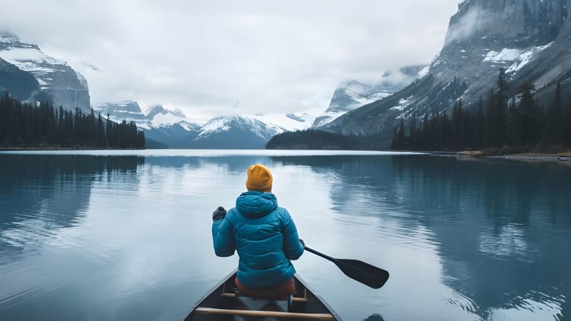 Eine Person in blauem Jacke und Hut paddelt ein Kanu auf einem spiegelglatten See mit verschneiten Bergen im Hintergrund auf dem Campus der Stanstead College.