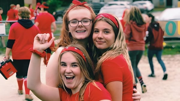 Drei Schülerinnen des Stayner Collegiate Institute tragen rote Shirts und lächeln vor einer Menschenmenge.