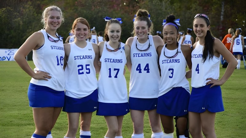 Sechs Schülerinnen in Sportuniformen der Stearns High School stehen draußen zusammen vor Bäumen und Grünflächen.