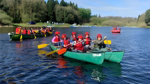Schüler der Stepaside Educate Together Secondary School paddeln mit roten Schwimmwesten farbenfrohe Kanus auf einem See.