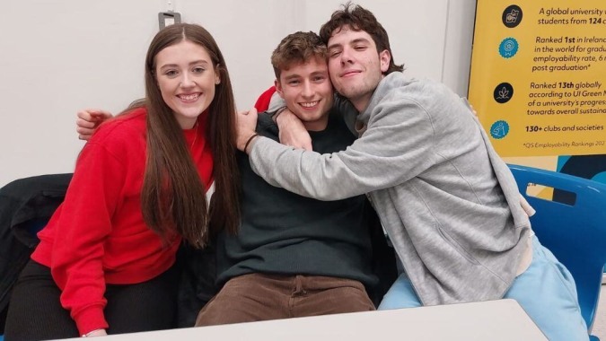 Drei Schülerinnen und Schüler umarmen sich und lächeln im Klassenzimmer der Stepaside Educate Together Secondary School.