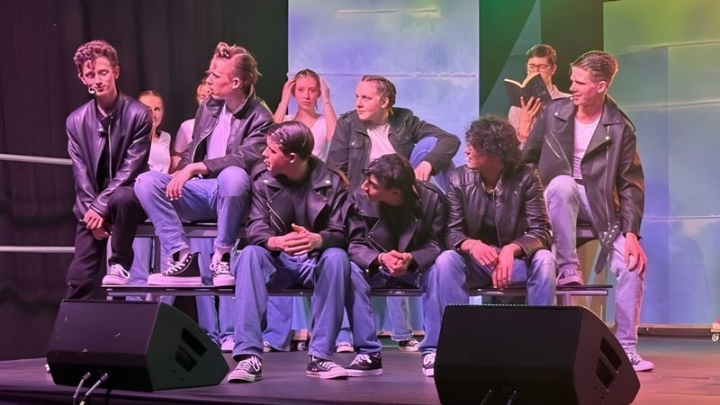 Eine Gruppe von Schülerinnen und Schülern sitzt auf der Bühne der Stepaside Educate Together Secondary School vor einem farbigen Bühnenhintergrund.