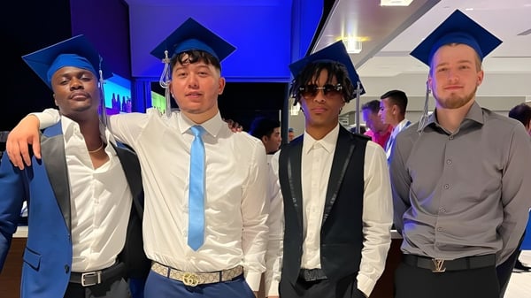 Eine Gruppe von Schülern der Stephen Lewis Secondary School steht zusammen in Abschlusskleidung vor blau-lila beleuchtetem Hintergrund.