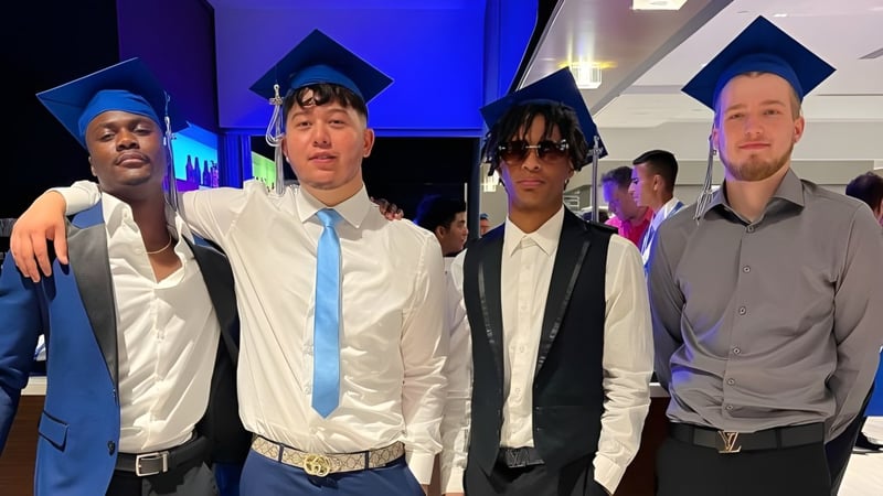 Eine Gruppe von Schülern der Stephen Lewis Secondary School steht zusammen in Abschlusskleidung vor blau-lila beleuchtetem Hintergrund.