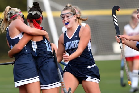 Schülerinnen der Stephen Perse Foundation spielen ein Feldhockeyspiel auf einem Rasenfeld.