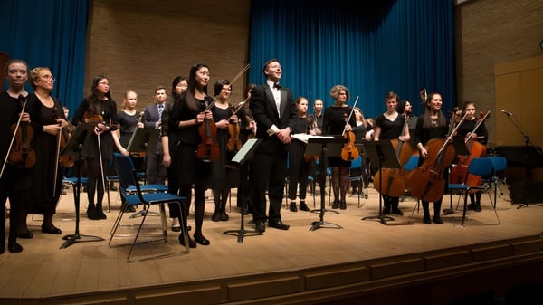 Das Orchester der Stephen Perse Foundation führt ein Konzert auf einer Bühne mit blauen Vorhängen auf.