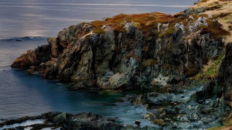 Steinige Klippen mit orange-grüner Vegetation ragen aus dem türkisfarbenen Wasser nahe der Stephenville High School auf.