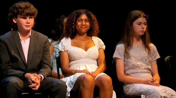 Drei Personen sitzen in formeller Kleidung auf einer Bühne bei einer Veranstaltung der Stevenson School.